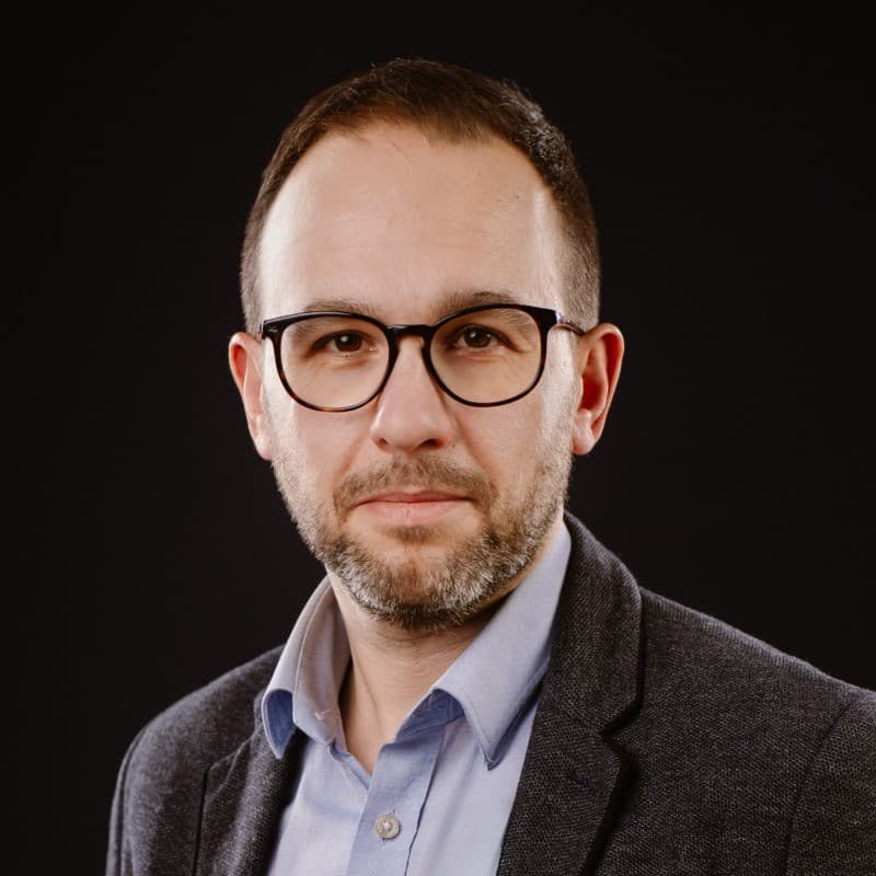 Andrzej Lemański – portret mężczyzny w okularach, marynarce i błękitnej koszuli na ciemnym tle.