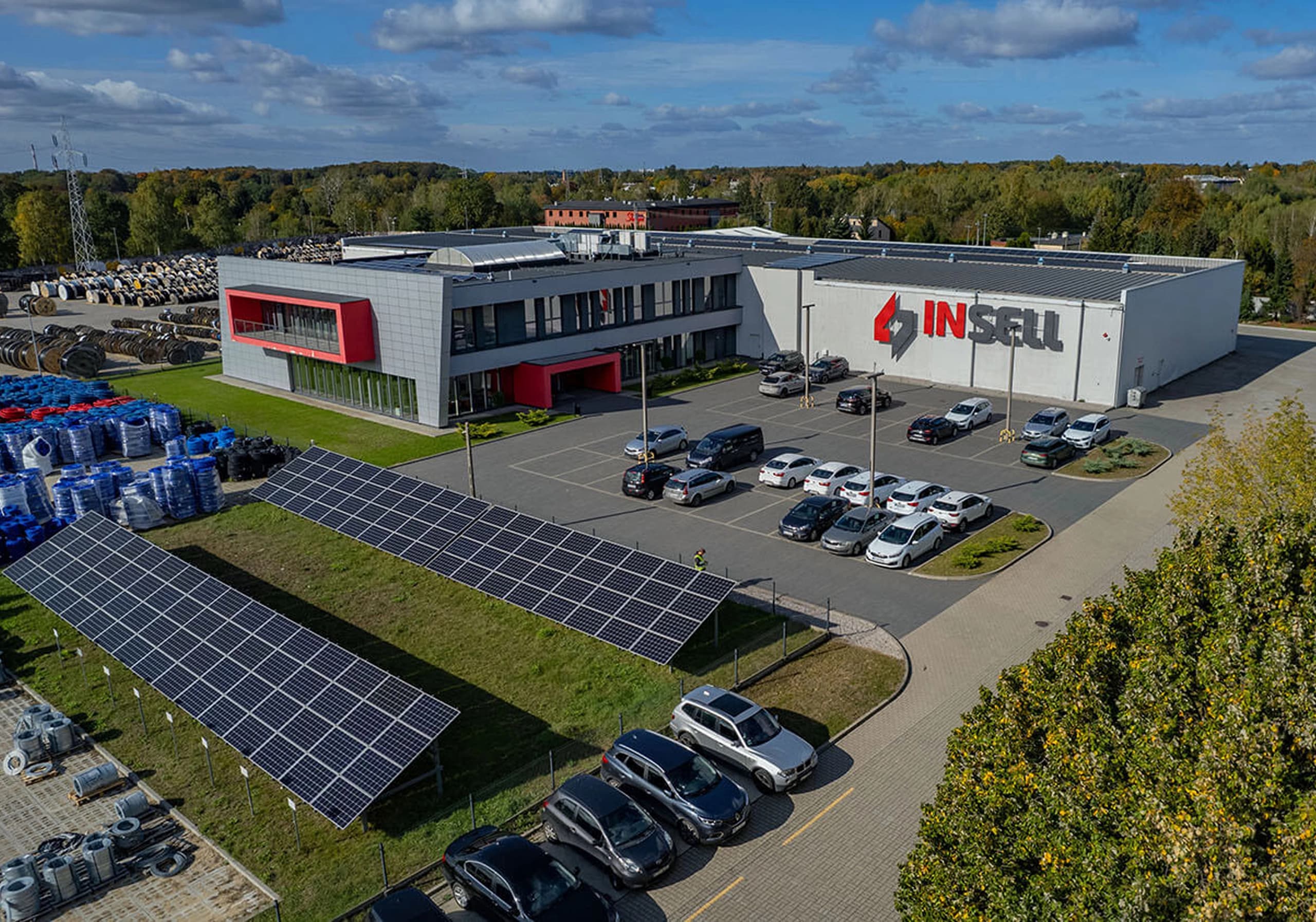 Siedziba firmy Insell widziana z lotu ptaka – budynek z logo INSELL, parking i panele fotowoltaiczne na pierwszym planie.