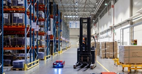 Wózek widłowy i autonomiczny robot AMR z niebieskim światłem w magazynie wysokiego składowania.