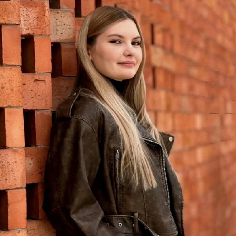 Ewelina Królikowska – młoda kobieta z długimi jasnymi włosami w skórzanej kurtce, oparta o ceglaną ścianę.
