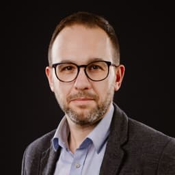 Andrzej Lemański – portret mężczyzny w okularach, marynarce i błękitnej koszuli na ciemnym tle.